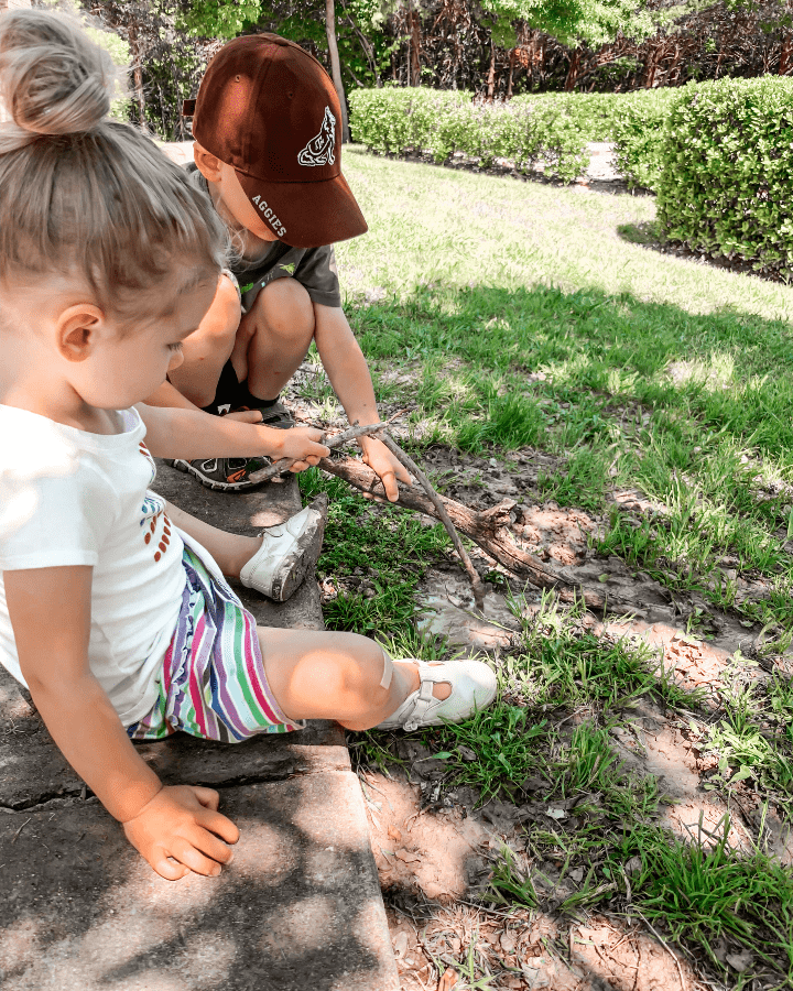 two children playing in the mud with a stick