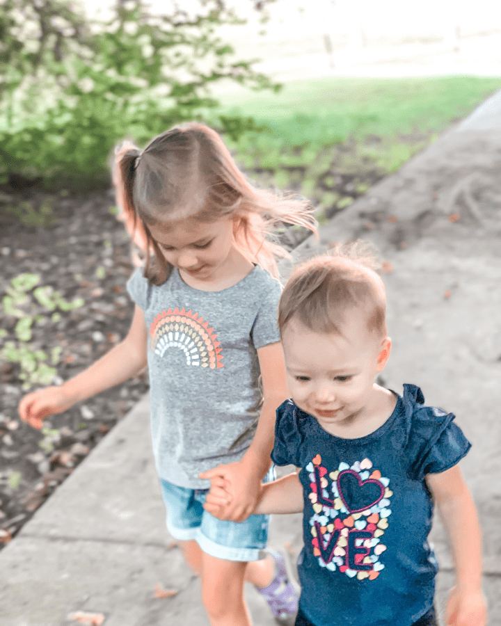 two little girls holding hands outside on the sidewalk